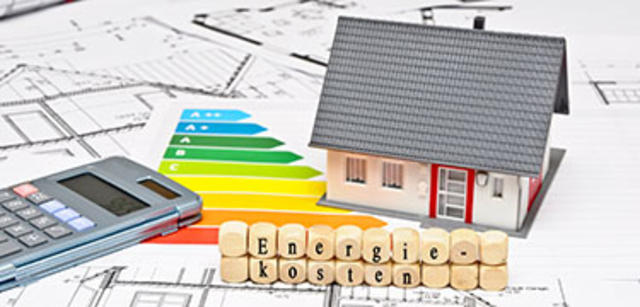 Modellhaus auf Bauplänen mit Energieeffizienzskala, Taschenrechner und Würfeln mit dem Wort Energiekosten